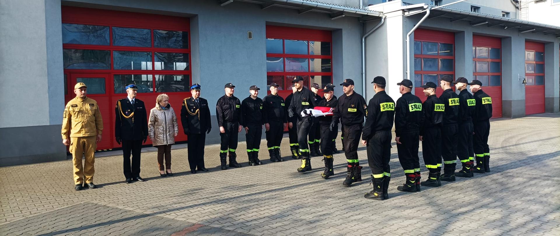 Na zdjęciu widoczni funkcjonariusze oraz pracownicy cywilni Komendy Powiatowej Państwowej Straży Pożarnej w Lęborku podczas uroczystego podniesienia flagi państwowej na maszt.