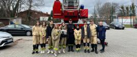 Grupowe zdjęcie uczestników wycieczki wraz ze strażakiem z KP PSP w Żyrardowie za tle rozłożonej w górę drabiny z wozu strażackiego