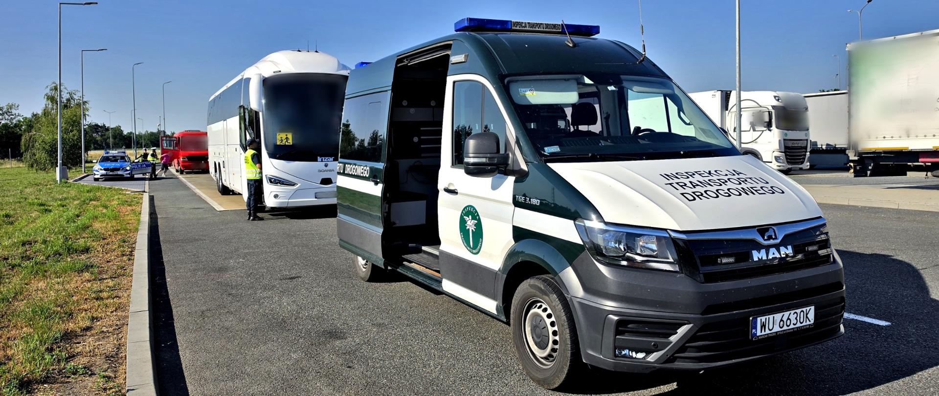Pojazd Inspekcji Transportu Drogowego i autokar podczas kontroli na parkingu przy drodze. W tle widoczne są ciężarówki i radiowóz policyjny.