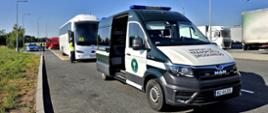Pojazd Inspekcji Transportu Drogowego i autokar podczas kontroli na parkingu przy drodze. W tle widoczne są ciężarówki i radiowóz policyjny.