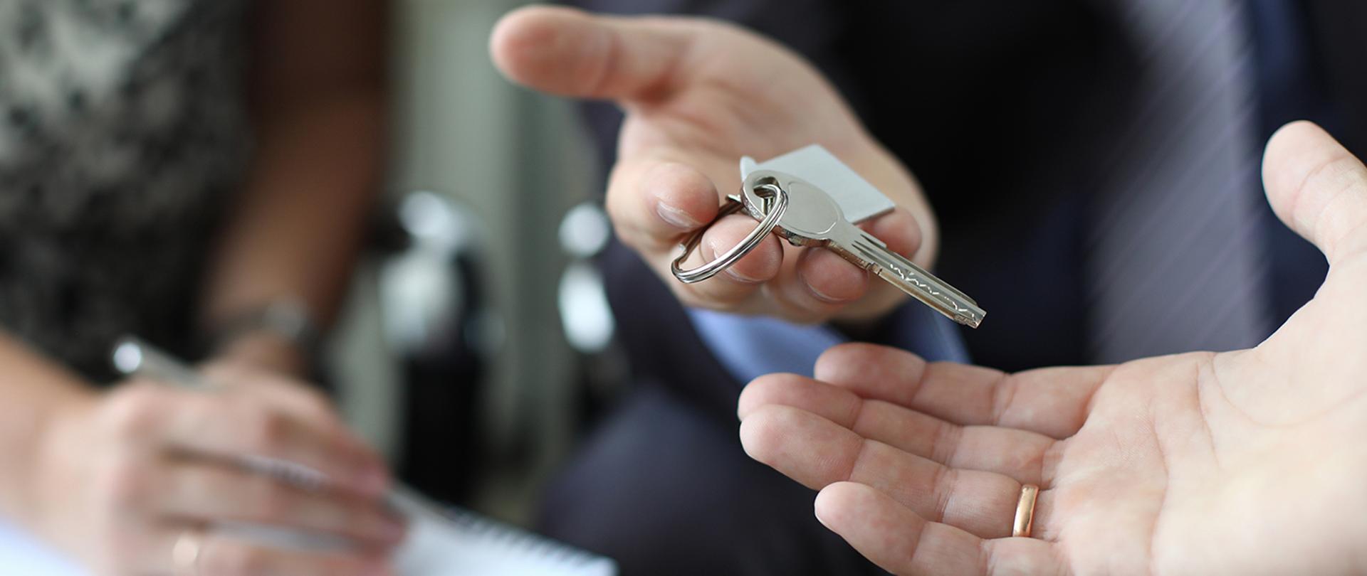 Realtor is handing over key of new apartment to couple after signing property insurance contract. Family mortgage concept.