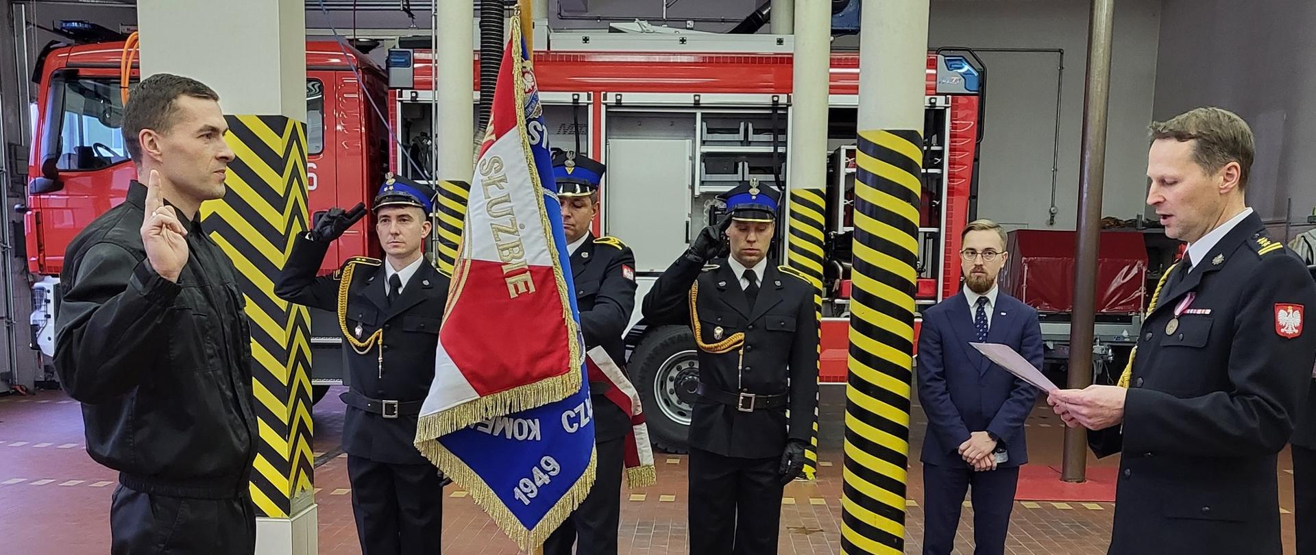 Komendant Powiatowy PSP w Człuchowie st. bryg. Ernest Szczepański przyjmuje ślubowanie składane przez str. Mariusza Strzeleckiego. W tle poczet sztandarowy i nowy samochód ratowniczo – gaśniczy.