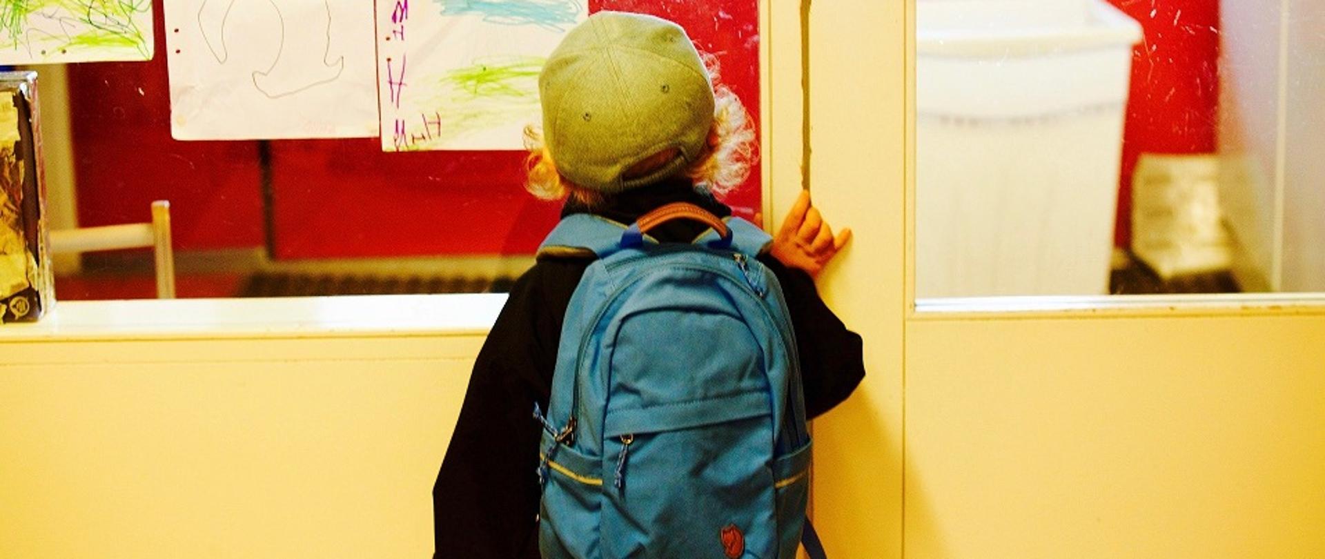 Mały chłopiec odwrócony tyłem z plecakiem na plecach, wchodzący do szkoły