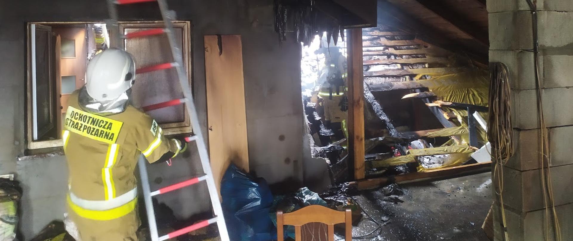 Zdjęcie przedstawia strażaka ochotnika w ubraniu specjalnym podczas akcji dogaszania dachu 