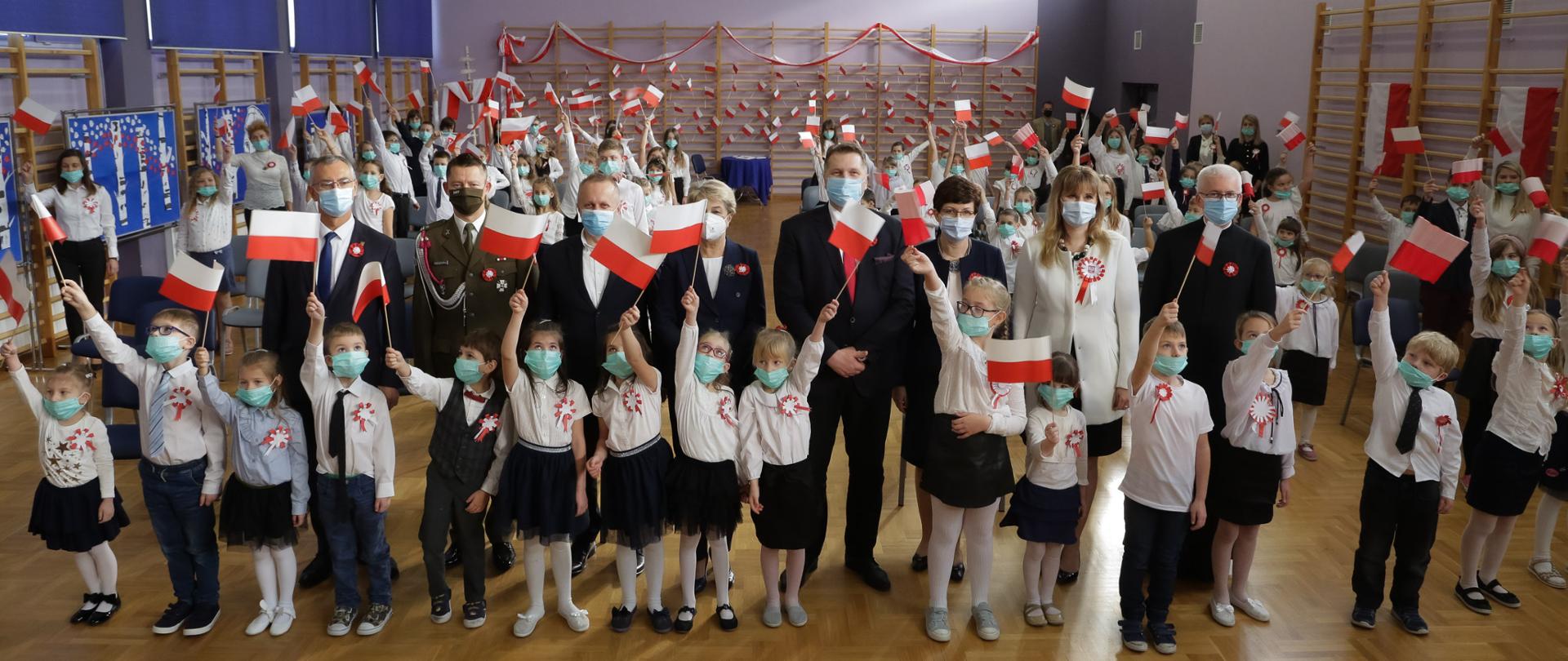 minister Przemysław czarnek podczas akcji szkoła do hymnu wraz z dziećmi i przedstawicielami szkoły pozuje do zdjecia na tle symboli narodowych 