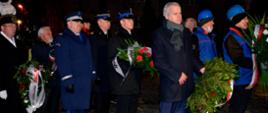 Przedstawiciele służb mundurowych stoją w kolejce do złożenia wieńca pod pomnikiem.