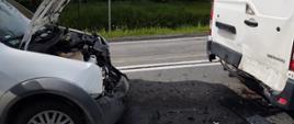 Przód rozbitego samochodu a przed nim tył samochodu dostawczego.