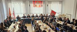 Widok ogólny sali OSP - na pierwszym planie uczestnicy zebrania siedzą przy stołach, na drugim planie goście siedzą za stołem prezydialnym