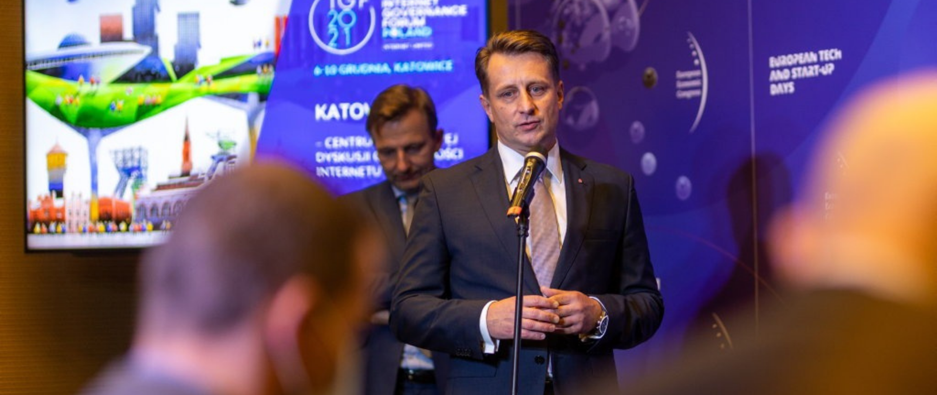 Krzysztof Szubert podczas konferencji prasowej w Katowicach, stoi przed mikrofonem, za nim prezydent Katowic.