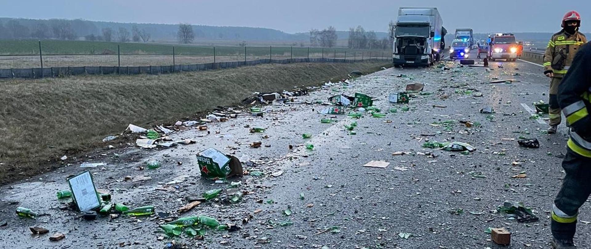 Na zdjęciu widać strażaków na drodze i rozrzucony towar z ciężarówki.