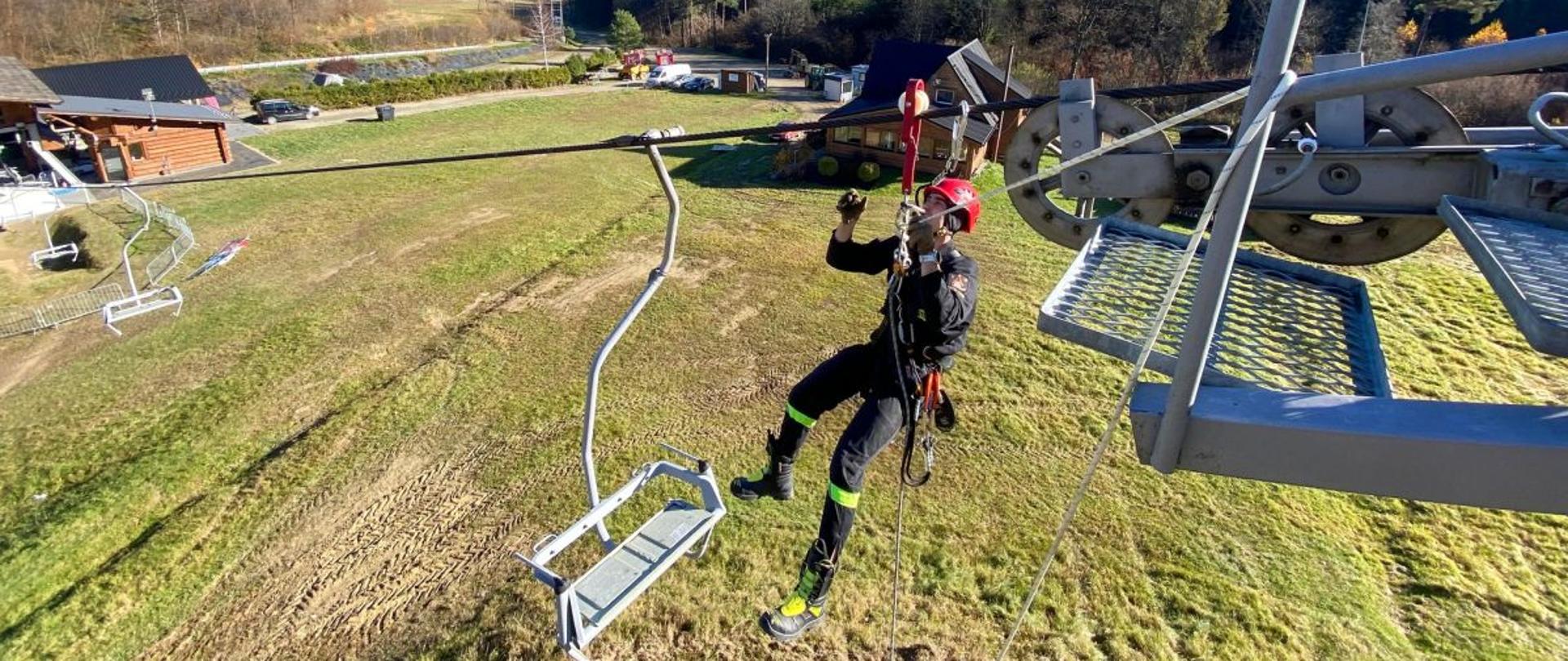 Zdjęcie przedstawia strażaka z JRG który wyposażony w sprzęt wysokościowy wisi na linii trakcyjnej wyciągu Laworta. 