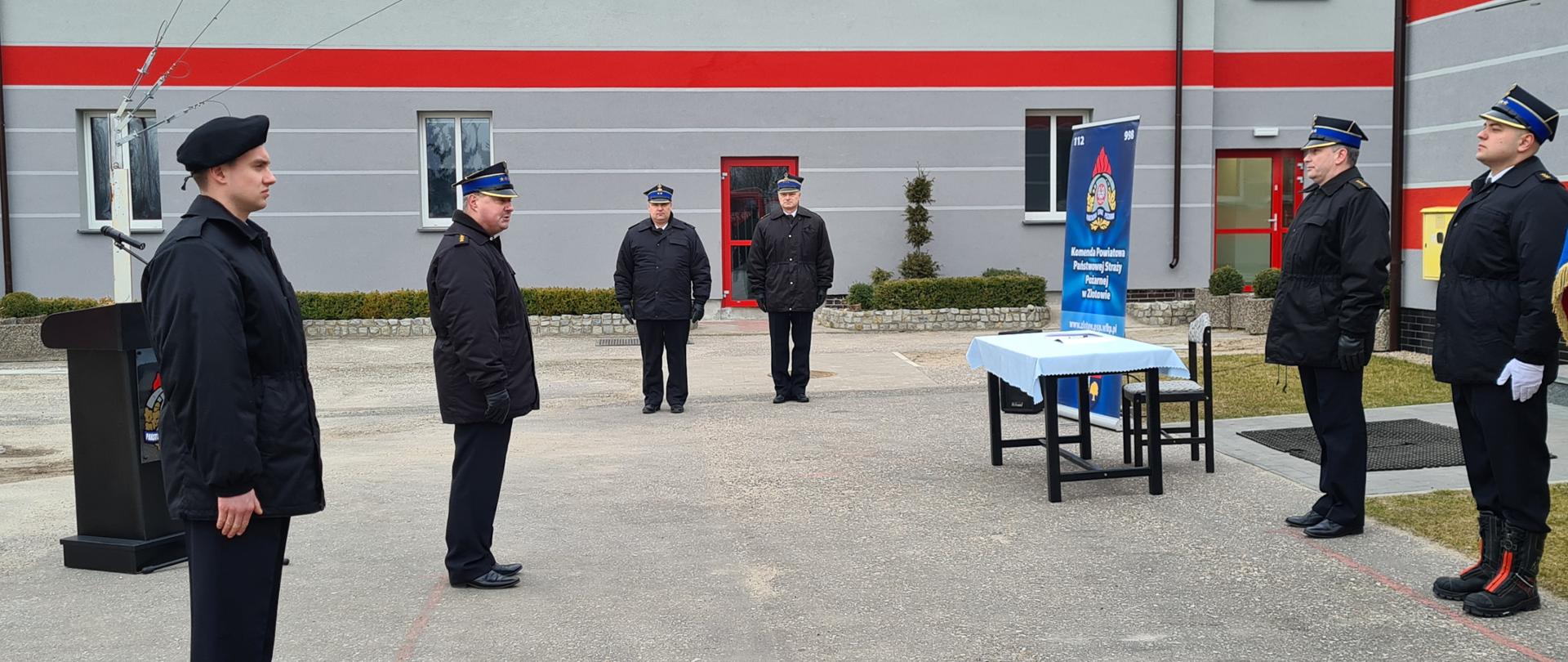  Na zdjęciu w tle zdjęcia widoczni są komendanci powiatowi bliżej kadru widzimy po lewej stronie zdjęcia dowódcę JRG a z przodu zdjęcia nowego strażaka