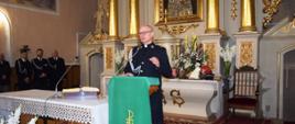 Wnętrze kościoła, ksiądz w mundurze strażackim w kolorze ciemnogranatowym przemawia z mównicy.