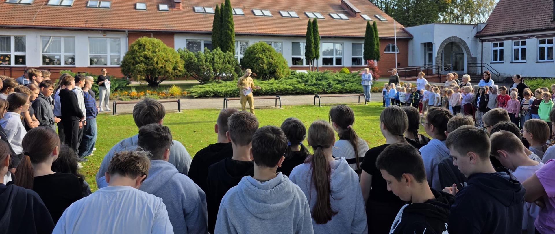 Funkcjonariusz PSP podczas omawiania przebiegu ewakuacji oraz pogadanki dla uczniów i kadry szkoły podstawowej.