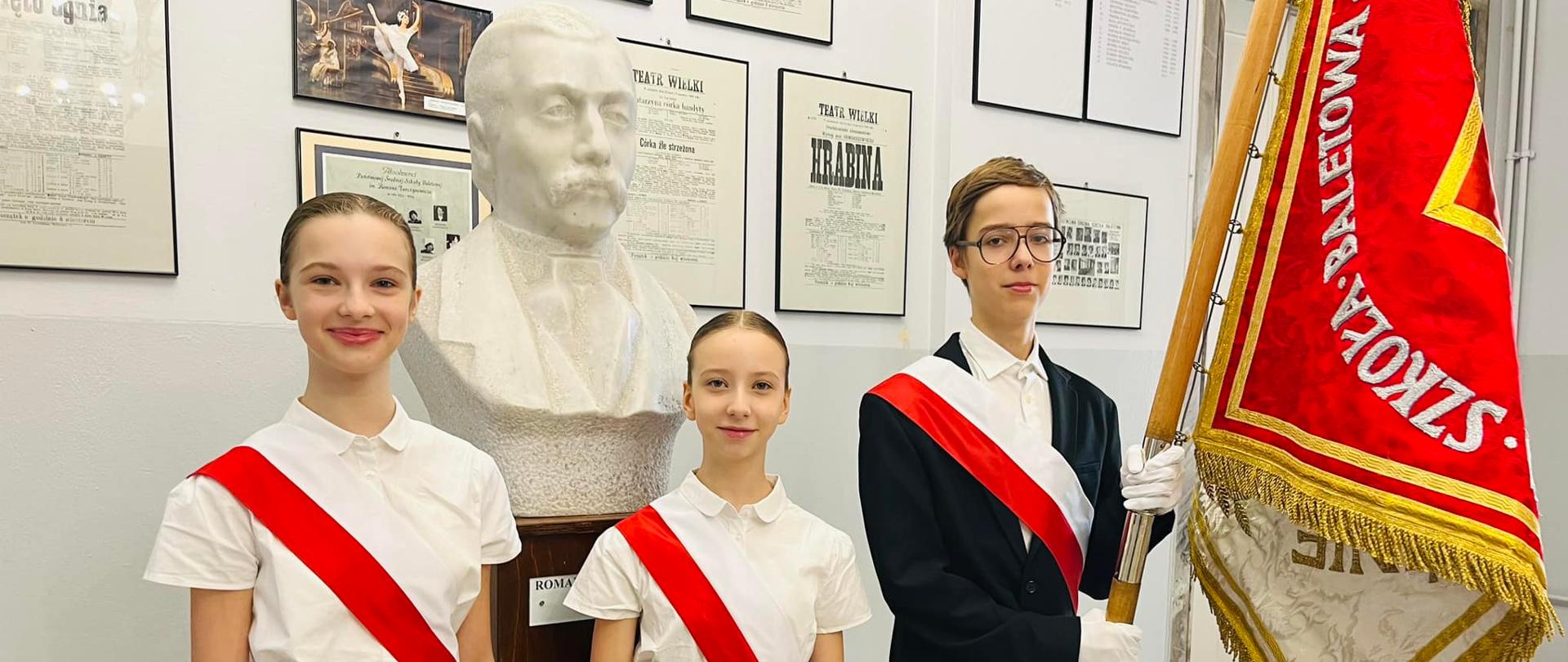 Zdjęcie uczniów reprezentujących poczet sztandarowy szkoły w holu patrona. Od lewej: Olivia Zyga, Alicja Brzozowa, Adam Tatarczak