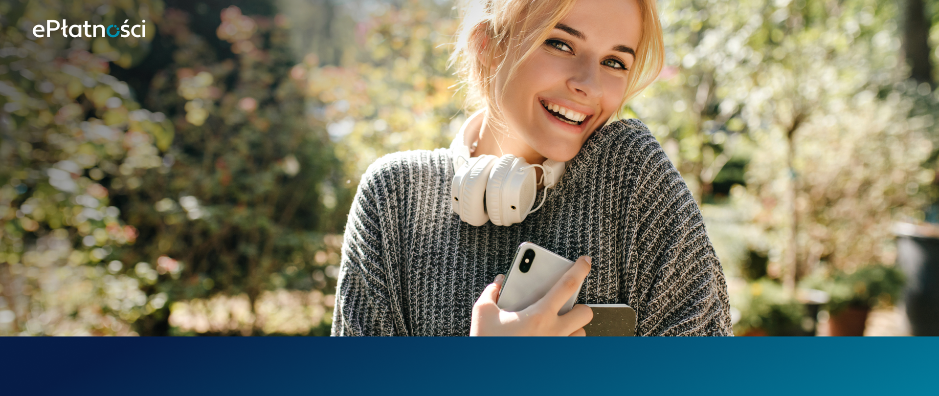 Uśmiechnięta blondynka z słuchawkami na szyi trzyma w prawej ręce telefon 