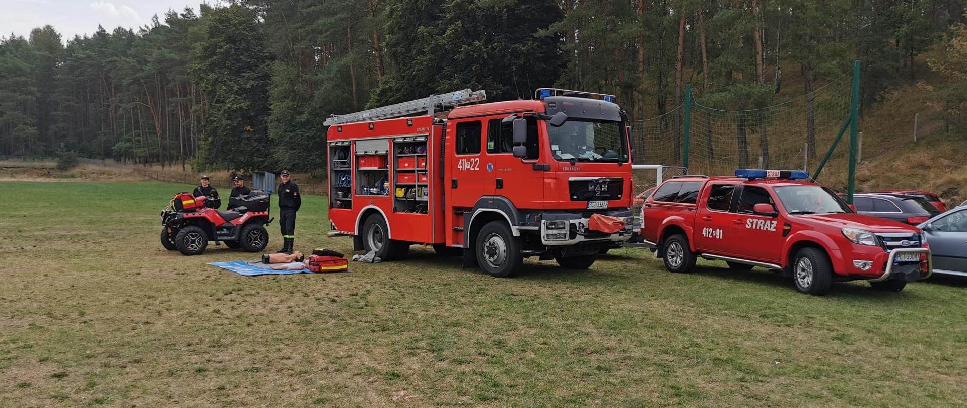 Przy wozach strażackich strażacy rozkładają sprzęt.