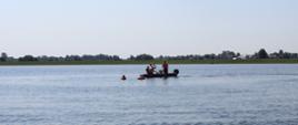 Zdjęcie przedstawia ratowników w łodzi motorowej na środku zbiornika podejmujących akcję ratowania osoby poszkodowanej z wody za pomocą koła ratunkowego 