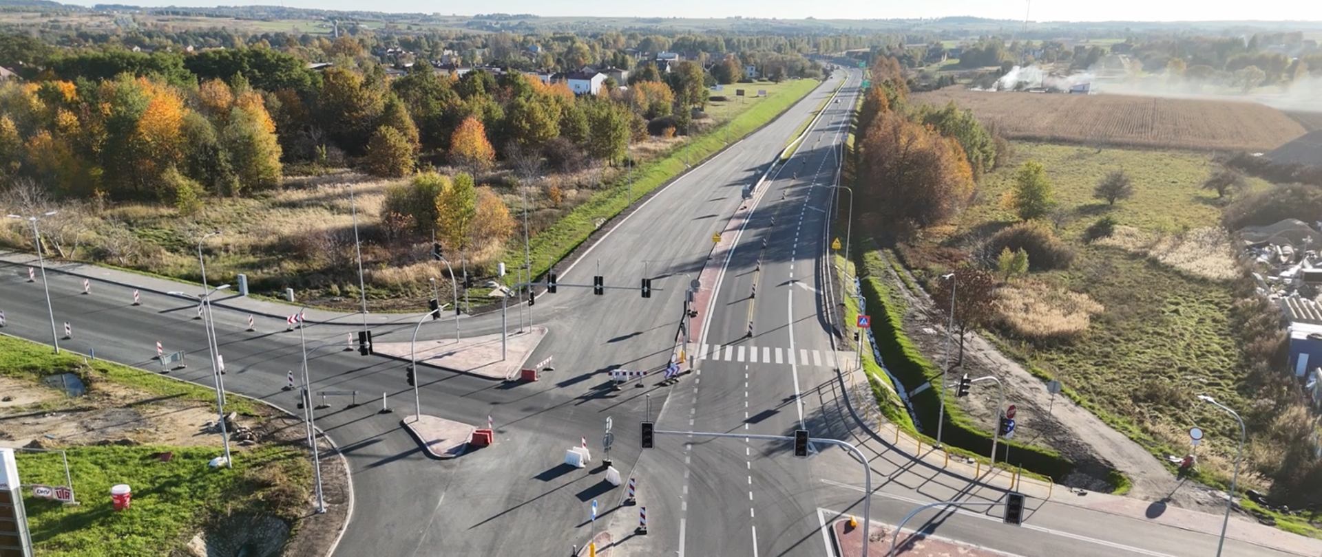 Widok z lotu ptaka na przebudowany odcinek drogi krajowej nr 91 pomiędzy Koziegłowami a Siedlcem Dużym. Na zdjęciu widać nową nawierzchnię jezdni, skrzyżowanie z sygnalizacją świetlną, oznakowane przejście dla pieszych oraz pasy ruchu. Po obu stronach drogi znajdują się tereny zielone i zabudowa rozproszona, w tle widoczny krajobraz pól i drzew w jesiennej kolorystyce.