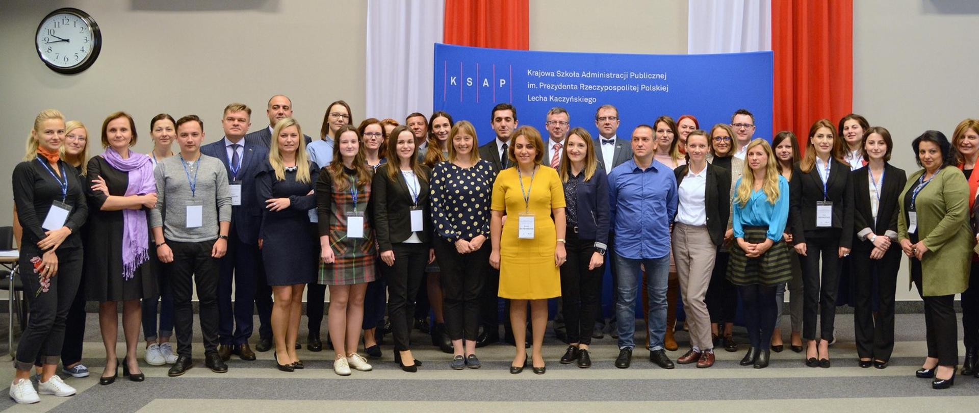 Grupa słuchaczy i wykładowców zgromadzona przed banerem Krajowej Szkoły Administracji Publicznej 2018