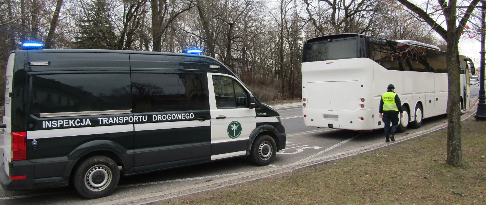 Kontrola drogowa białego autokaru prowadzona przez Inspekcję Transportu Drogowego przy zadrzewionej drodze.