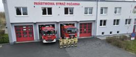 Zdjęcie wykonane w dzień. Przed budynkiem Komendy stoją dwa wozy strażackie. Przed wozami zmiana oddająca hold ofiarom katastrofy Smoleńskiej. Strażacy ubrani w piaskowe mundury i czerwone hełmy.
