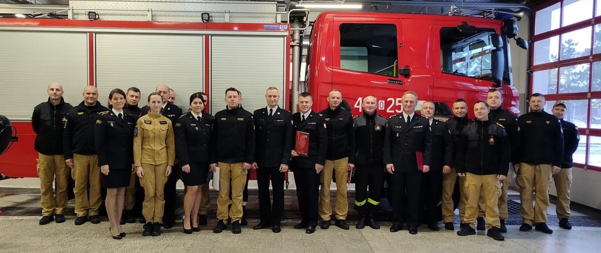 Na zdjęciu znajdują się strażacy w mundurach ustawieni do zdjęcia na tle podnośnika