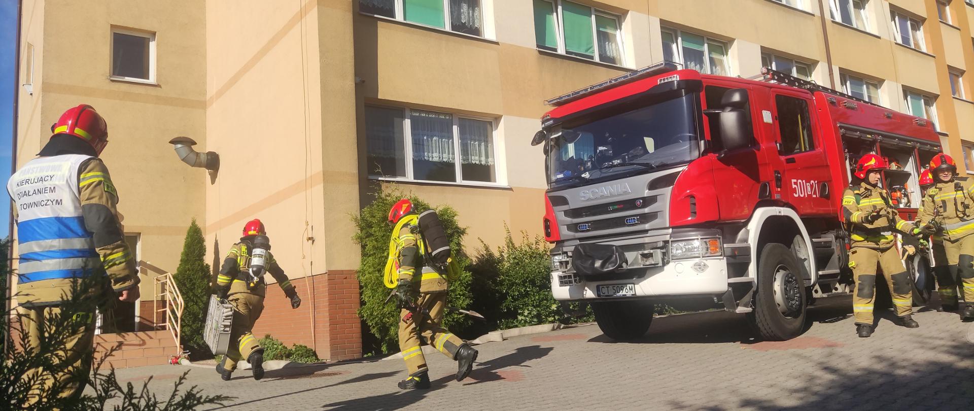 Zdjęcie przedstawia budynek Specjalnego Ośrodka Szkolno-Wychowawczego w Radziejowie, wóz bojowy straży pożarnej oraz strażaków podczas ćwiczeń obiektowych. 