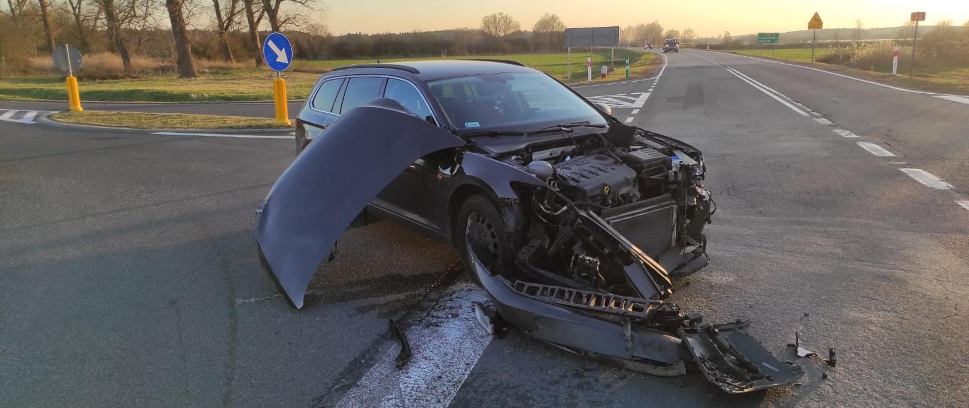 Zdjęcie przedstawia samochód osobowy stojący częściowo na drodze krajowej nr 32, który ma uszkodzony przód pojazdu w wyniku kolizji drogowej.