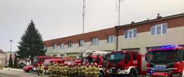 Strażacy stojąc na baczność na tle samochodów gaśniczych oddają cześć poległym strażakom z Ukrainy.
