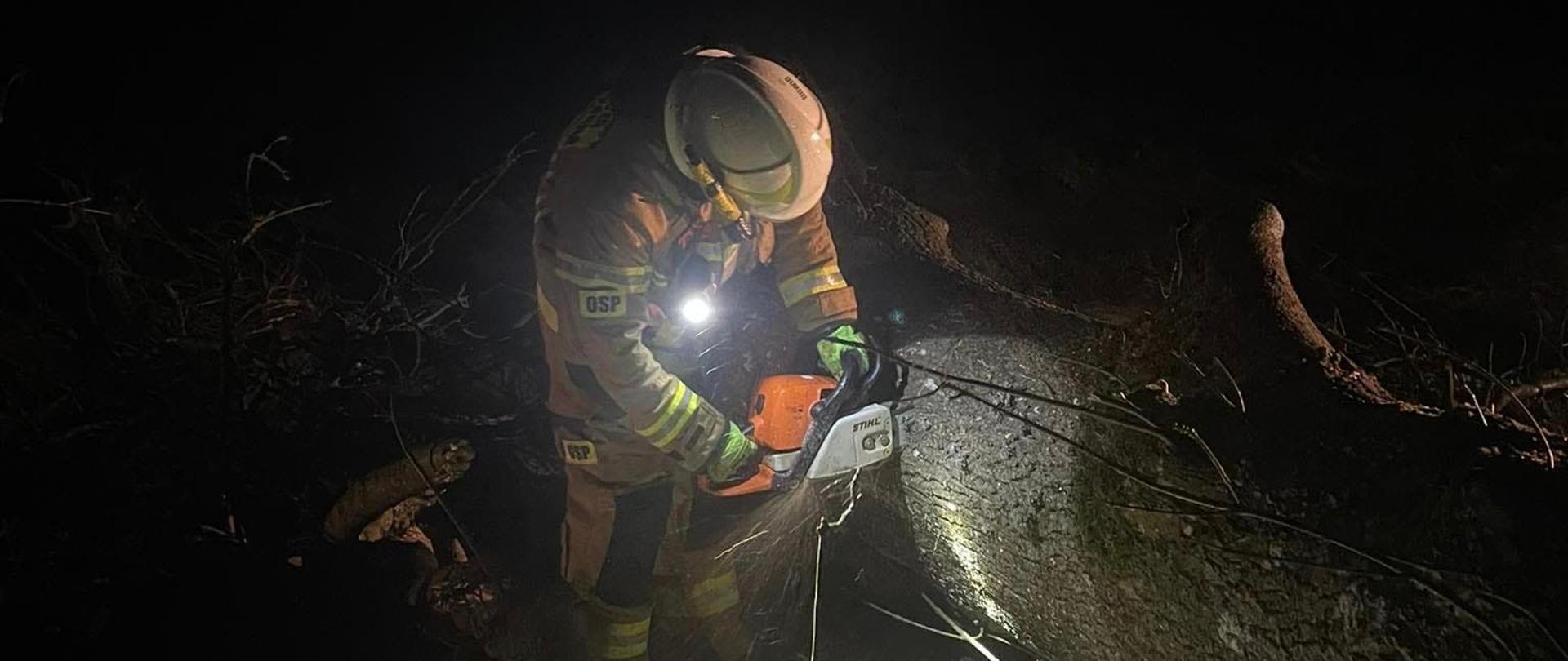 Strażak przecinający drzewo przewrócone na jezdnię