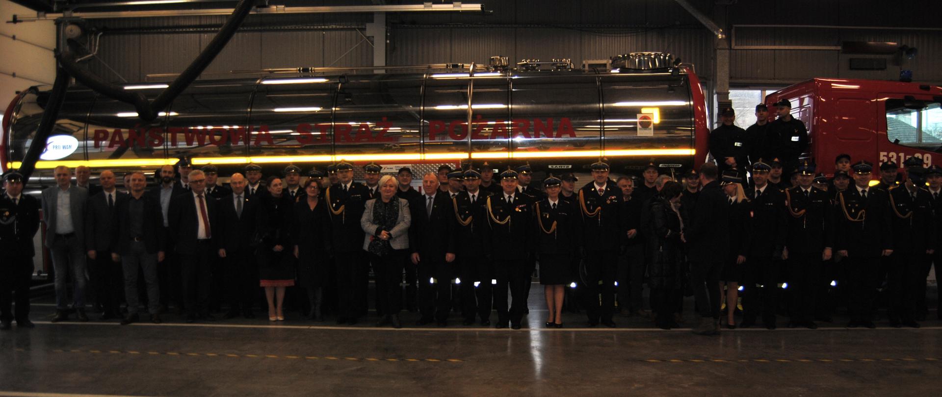 Zdjęcie grupowe gości na tle cysterny pożarniczej.