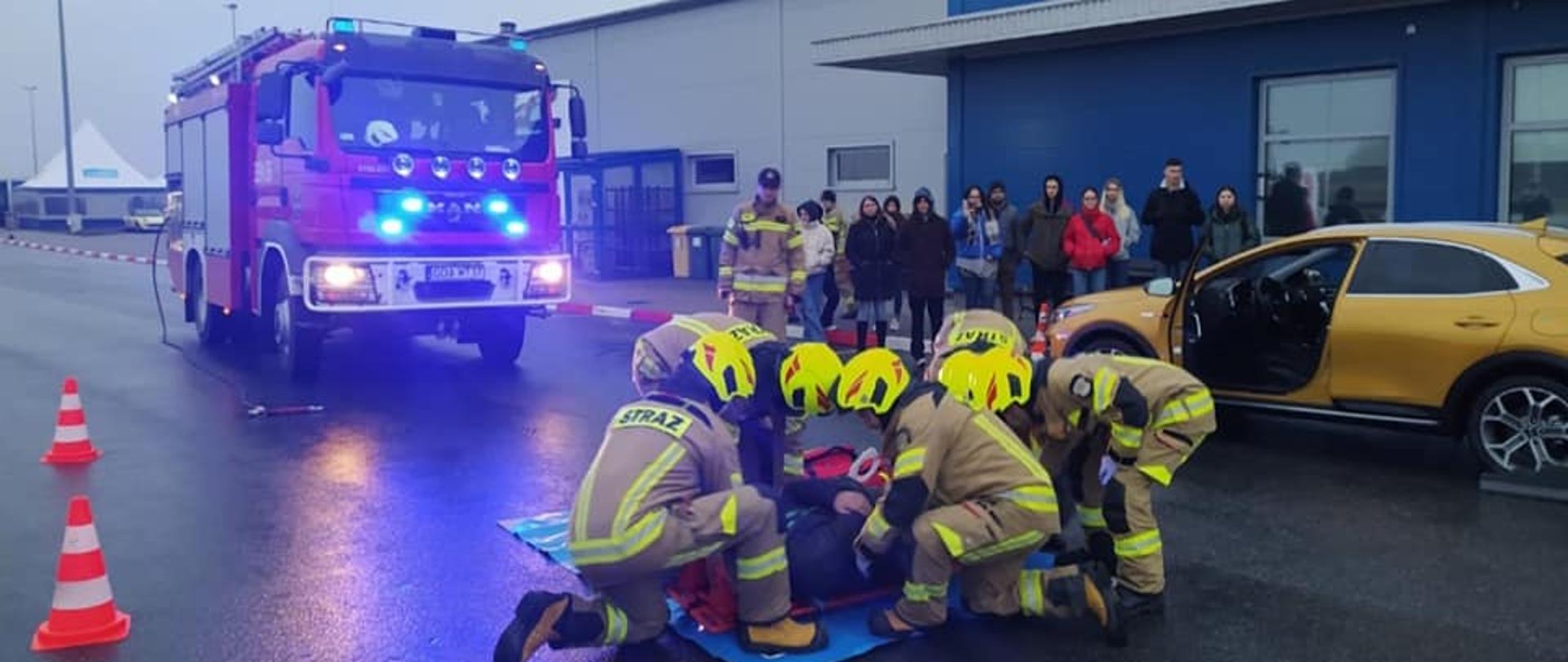 Zdjęcie przedstawia strażaków udzielających pomocy medycznej poszkodowanemu w symulowanym wypadku