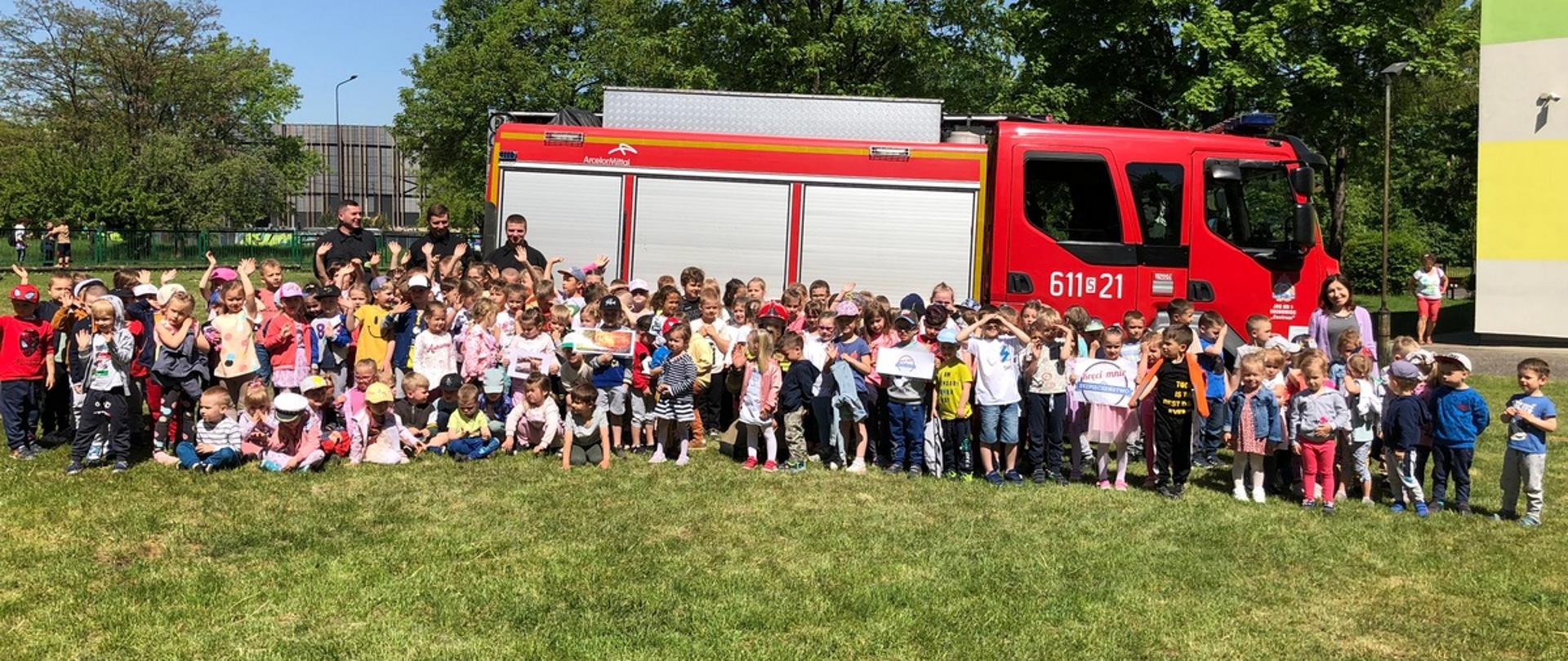 Na zdjęciu dzieci oraz funkcjonariusze Państwowej Straży Pożarnej na tle samochodu strażackiego