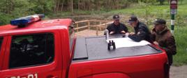Strażacy i pracownik nadleśnictwa analizują mapę rozłożoną na samochodzie.