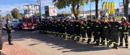 Zdjęcie przedstawia uczestników szkolenia. Strażacy ustawieni w dwuszeregu, umundurowani, w tle samochód pożarniczy