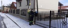 Strażak OSP wkładający ulotkę do skrzynki na listy przy bramie wjazdowej na posesję.