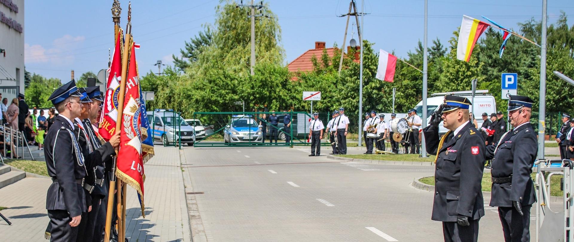 strażak stoi na baczność przed pocztem sztandarowym, za nim stoi drugi strażak 
