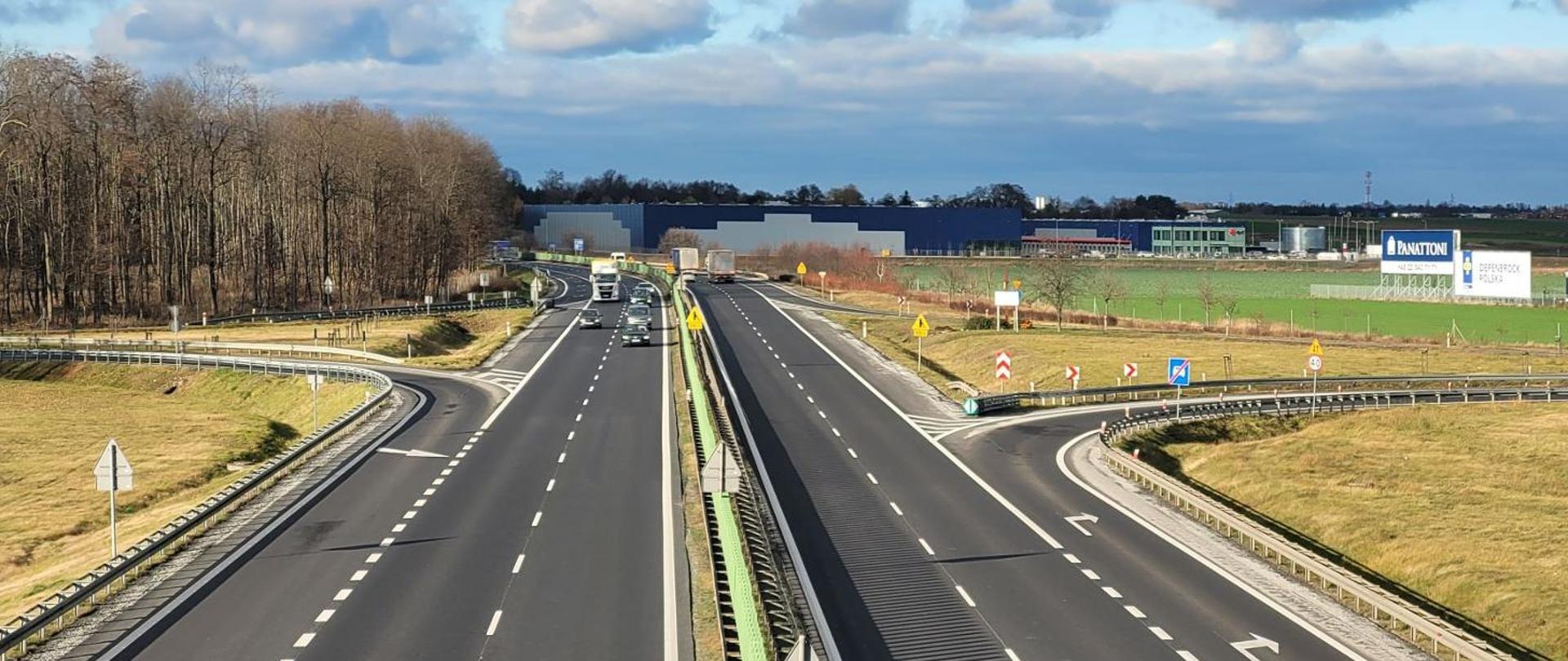 Droga ekspresowa dwujezdniowa, w tle zabudowania przemysłowe.