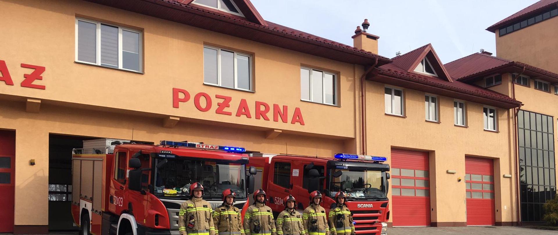 Zdjęcie przedstawia budynek Komendy Powiatowej PSP w Przeworsku, na tle którego odbyła się zbiórka strażaków z okazji upamiętnienia katastrofy w Smoleńsku Strażacy stoją w rzędzie a za nimi dwa samochody bojowe . 