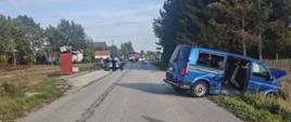 Przedstawia szeroki plan drogi objętej działaniami służb ratunkowych.Po prawej stronie w rowie stoi wspomniany wcześniej niebieski van, a w głębi drogi widać radiowozy policyjne i inne pojazdy służb. 