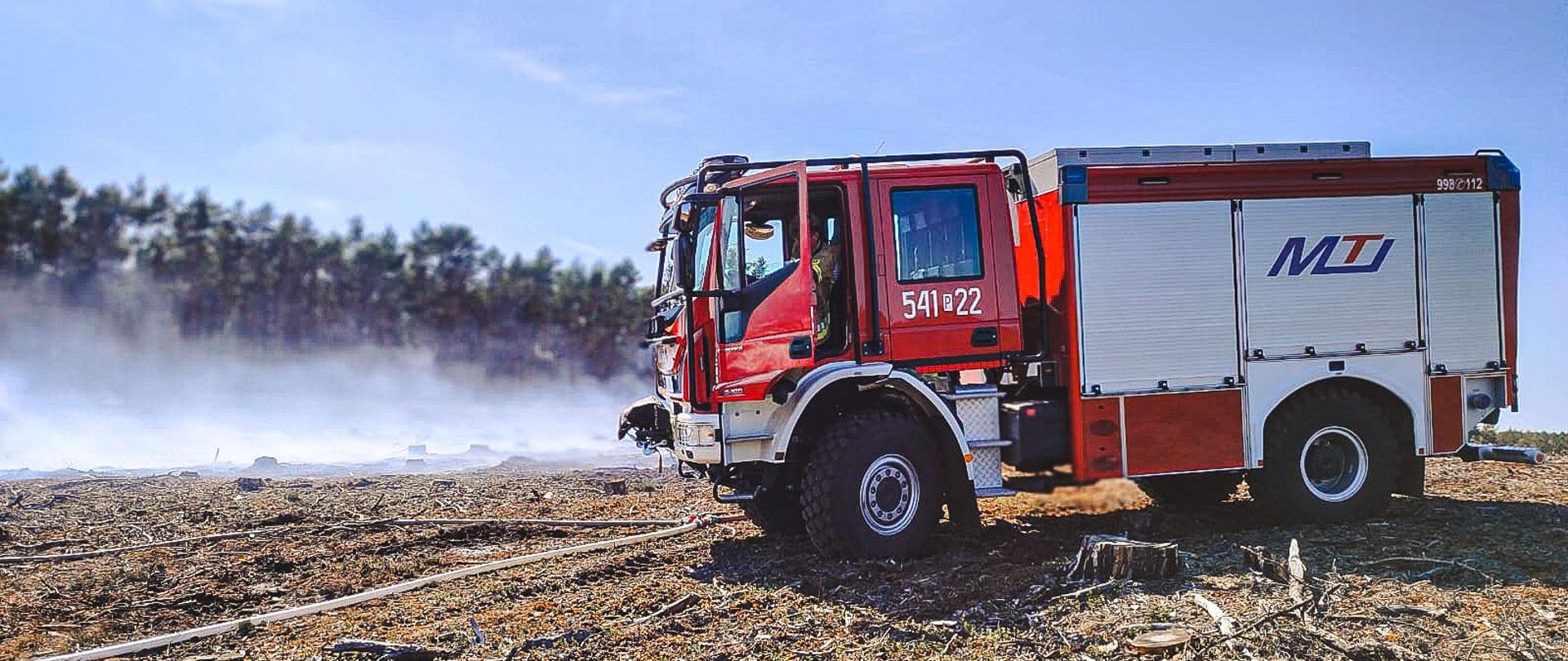 Wóz strażacki stojący w pobliżu pożaru. W tle las.