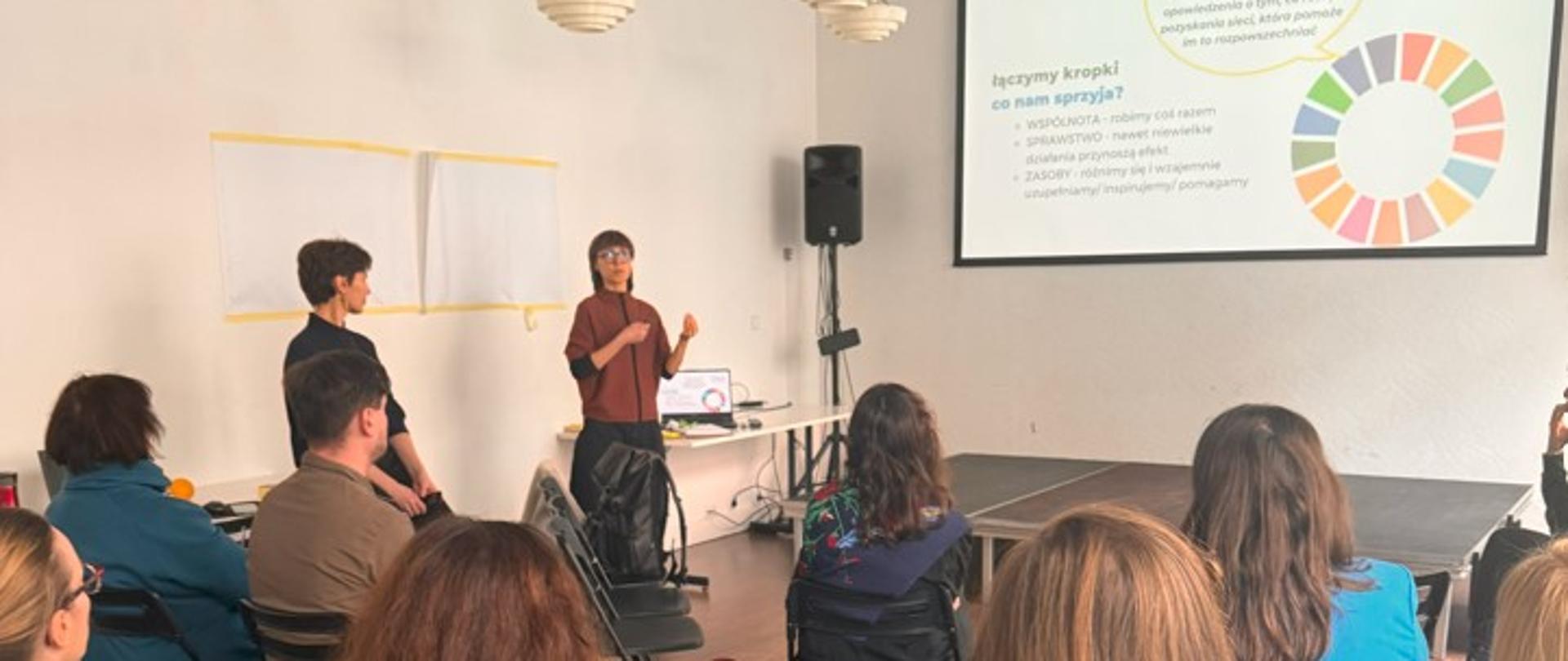 Ludzie siedzą na krzesłach i słuchają osoby prowadzącej szkolenie