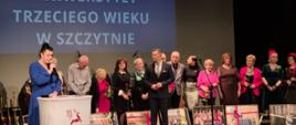 na zdjęciu duża grupa osób stojąca na scenie miejskiego domu kultury w tle prezentacja stowarzyszenia uniwersytetu trzeciego wieku