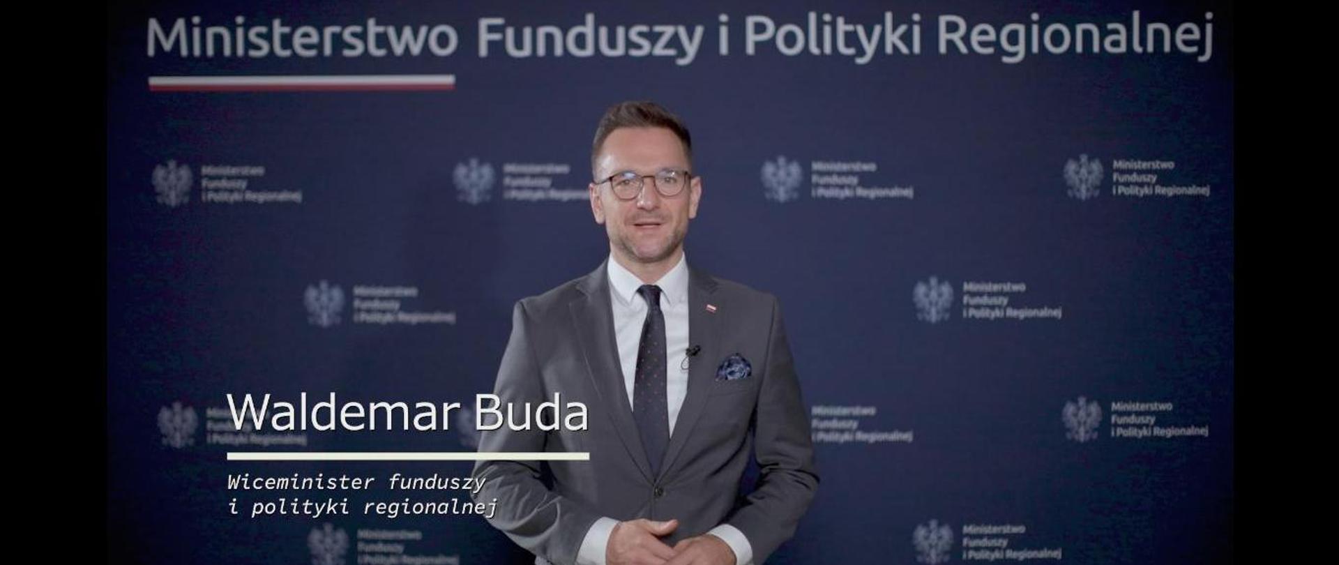 Zdjęcie wiceministra funduszy i polityki regionalnej Waldemara Budy na tle "ścianki" z logo resortu.