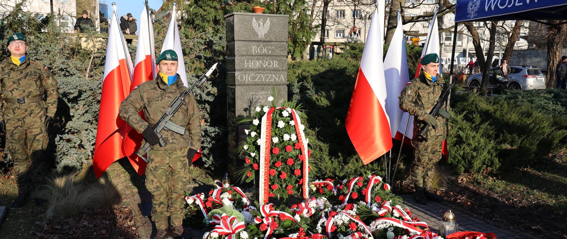 Pomnik z wartą honorową. Pod pomnikiem znajdują się wieńce i wiązanki kwiatów. 