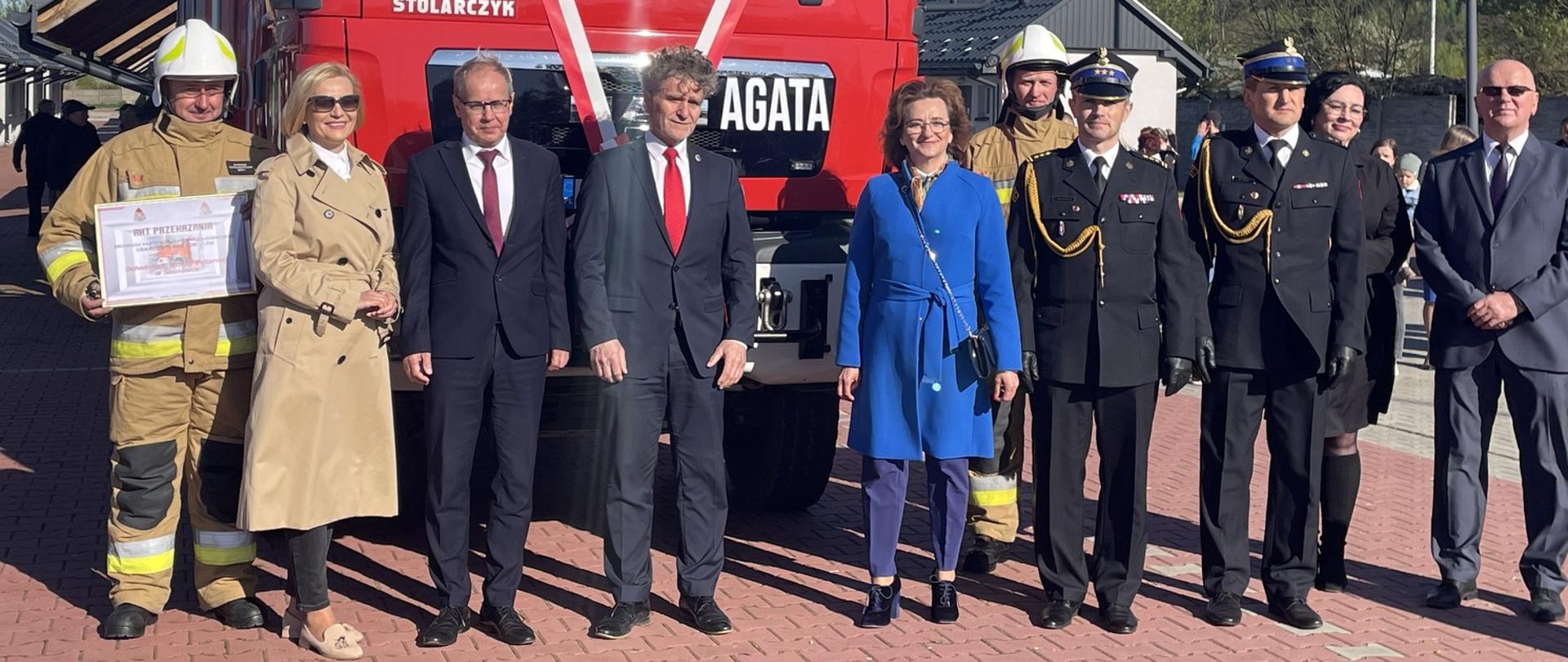 Zdjęcie przedstawia zaproszonych gości i organizatorów uroczystości stojących na tle nowo-pozyskanego wozu pożarniczego.