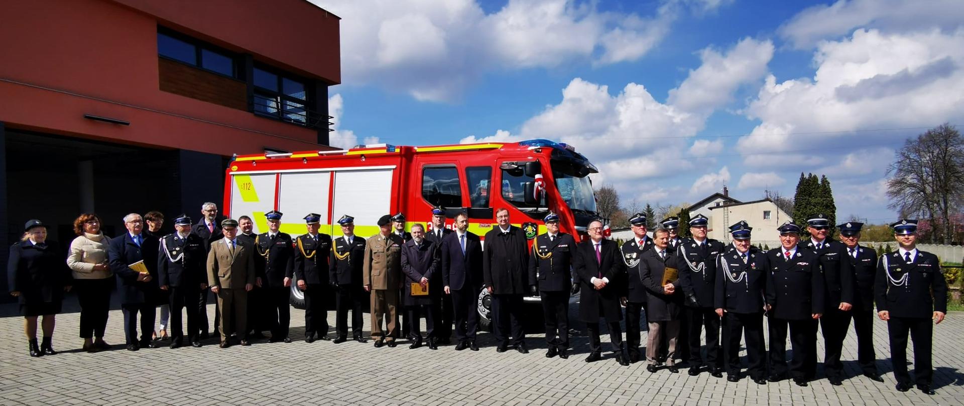 Zdjęcie grupowe uczestników uroczystego przekazania samochodu ratowniczo-gaśniczego stojących na tle nowego pojazdu.