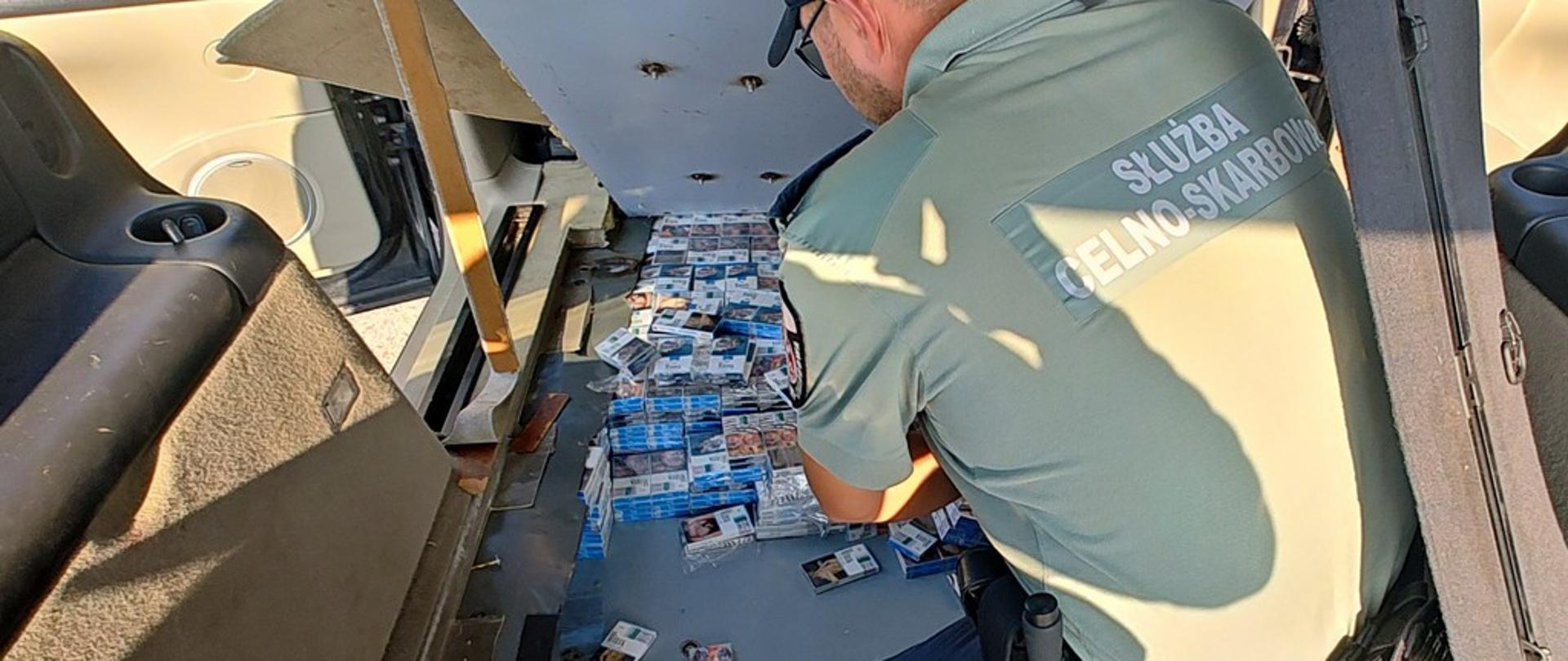 Funkcjonariusz wyjmuje papierosy z podłogi auta
