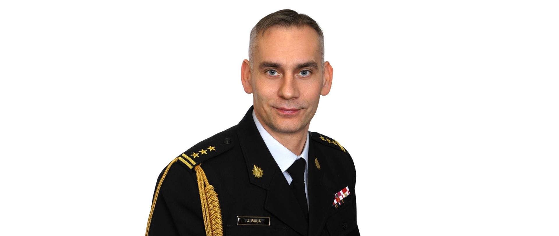 Zdjęcie portretowe na jasnym tle komendanta Powiatowego Państwowej Straży Pożarnej w Lublińcu starszy brygadier Janusz Bula w mundurze galowym.
